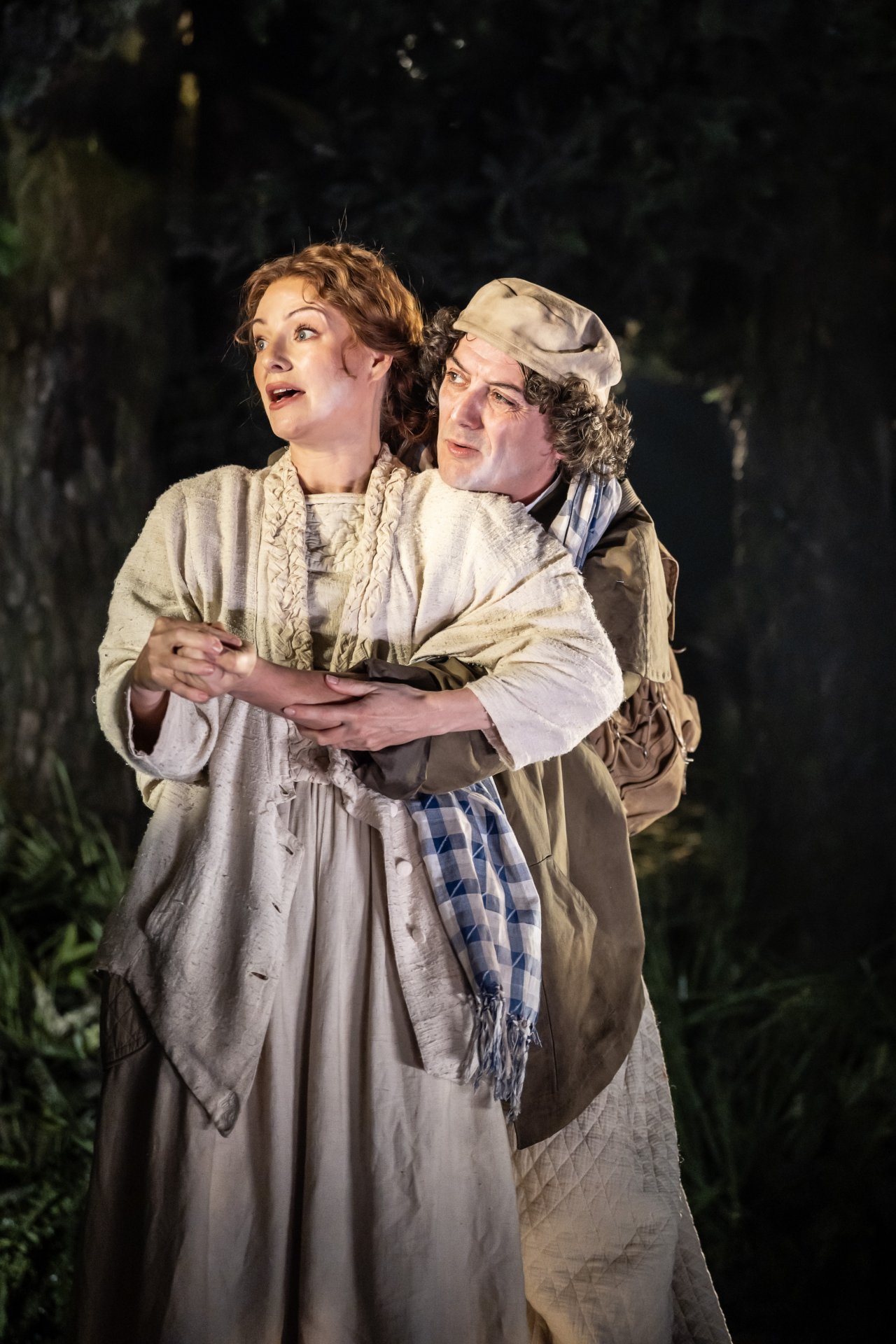 The Baker and the Baker's Wife stand close together in the woods, looking off into the distance, in Into the Woods. The Baker and the Baker's Wife stand close together in the woods, looking off into the distance, in Into the Woods.