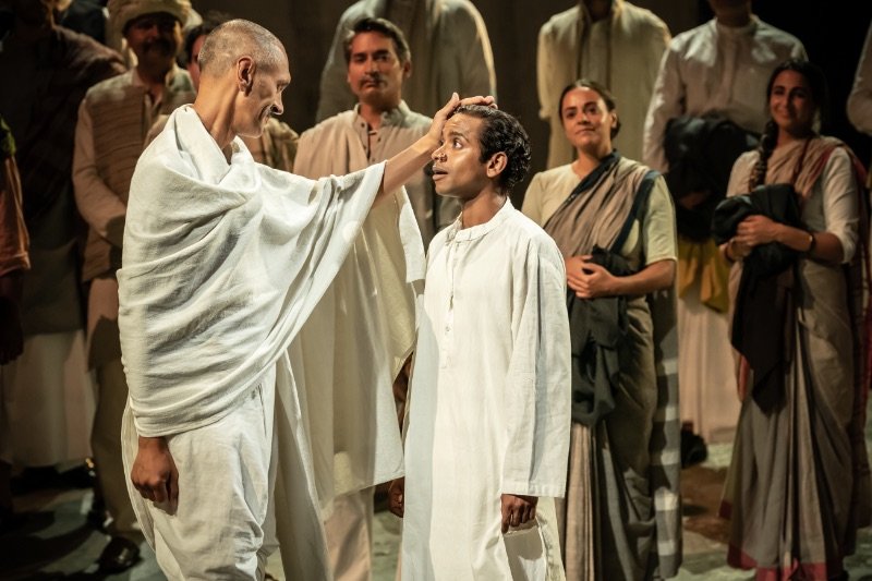 Paul-Bazely-Mohandas-Gandhi-Hiran-Abeysekera-Nathuram-Godse-and-The-Father-and-the-Assassin-company-at-the-National-Theatre-2023.-Credits-Marc-Brenner Paul-Bazely-Mohandas-Gandhi-Hiran-Abeysekera-Nathuram-Godse-and-The-Father-and-the-Assassin-company-at-the-National-Theatre-2023.-Credits-Marc-Brenner