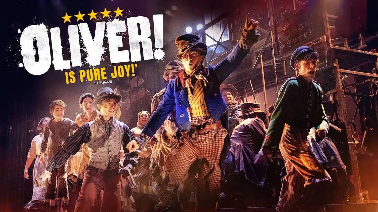 Promotional image of the Oliver! stage musical: a lively chorus in vintage costumes performing on a theater set with bold title text 'OLIVER! IS PURE JOY!'