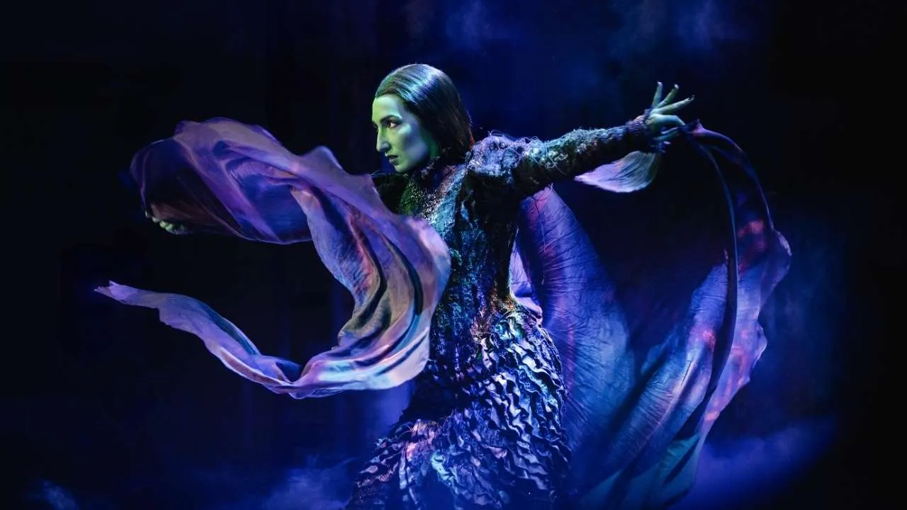 A woman stands in a swirl of fabric, highlighted by blue and purple lights.