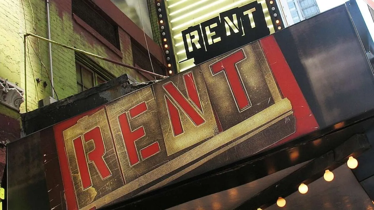 Theater marquee with bold red letters spelling RENT against a dark storefront.