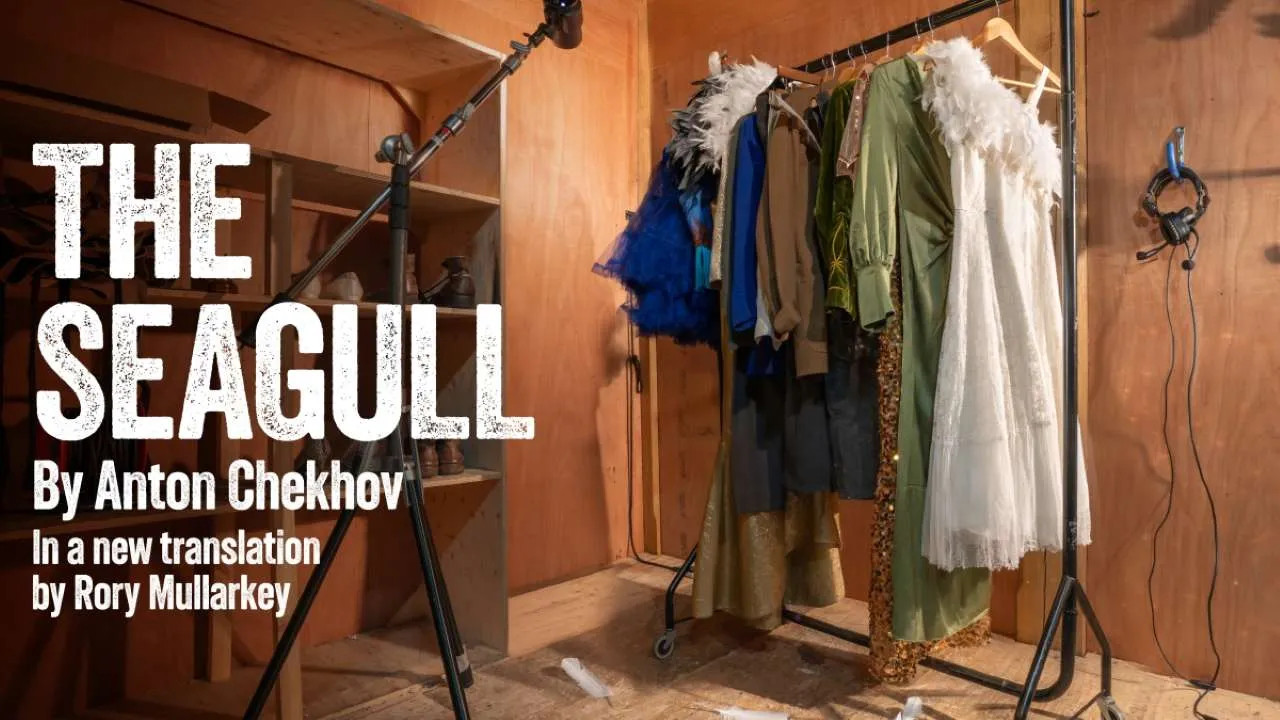 The Seagull theater poster with large title on the left and costumes on a rack in a backstage wood-paneled room on the right.
