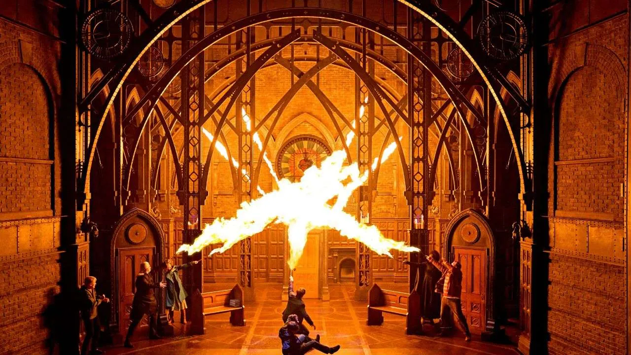 Fiery performance in a grand Gothic hall with arched pillars and spectators nearby while performers shoot flames between them across the room.