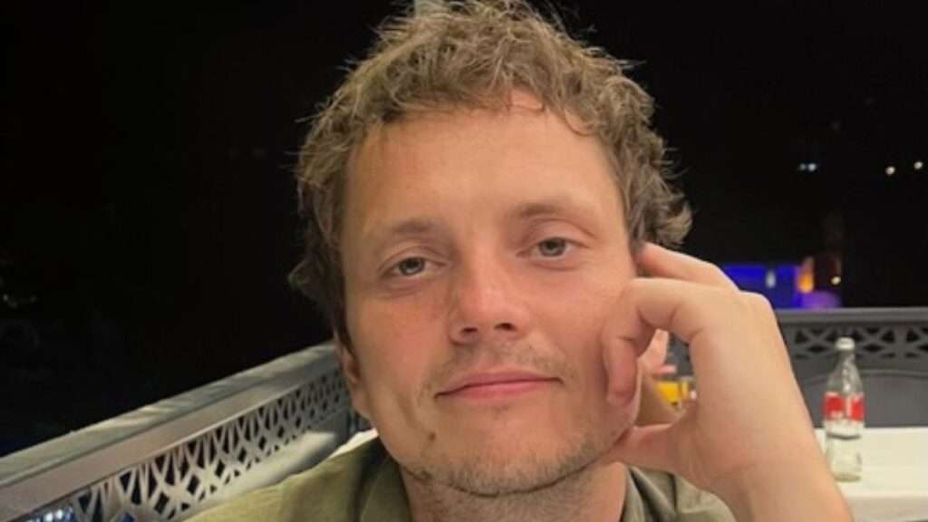 Relaxed man with tousled hair resting his head on his hand at night on a balcony.