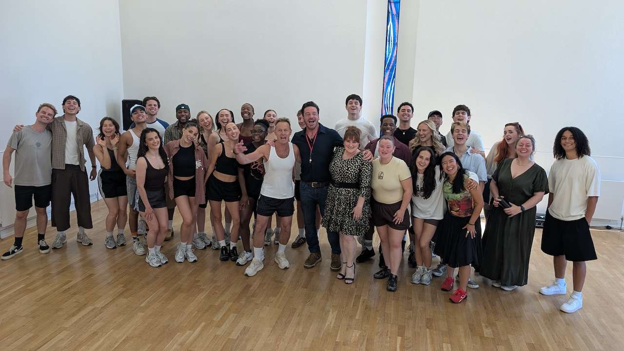 Large diverse group posing together in a bright dance studio with wooden floors.