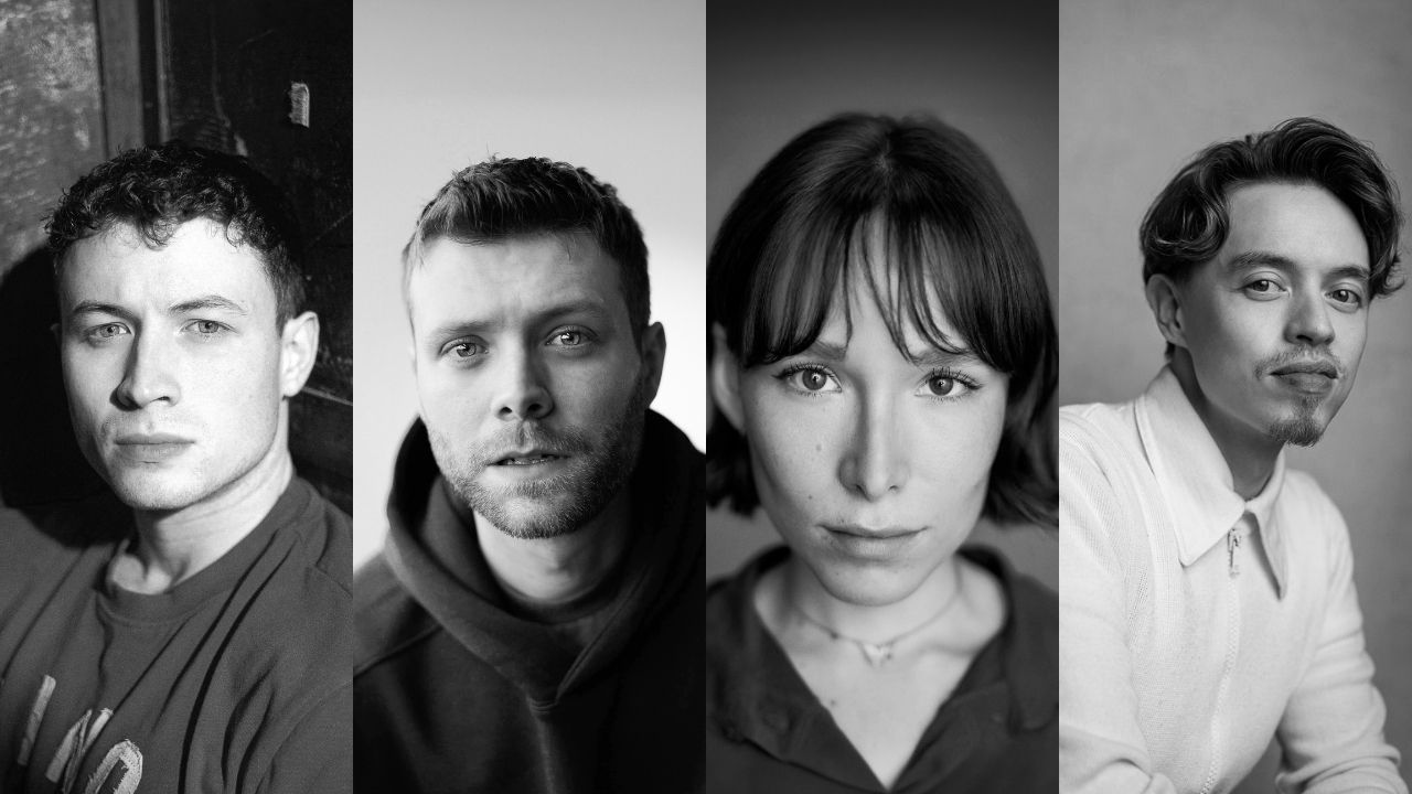 Black-and-white group portrait of four adults looking at the camera, standing side by side against a neutral background.