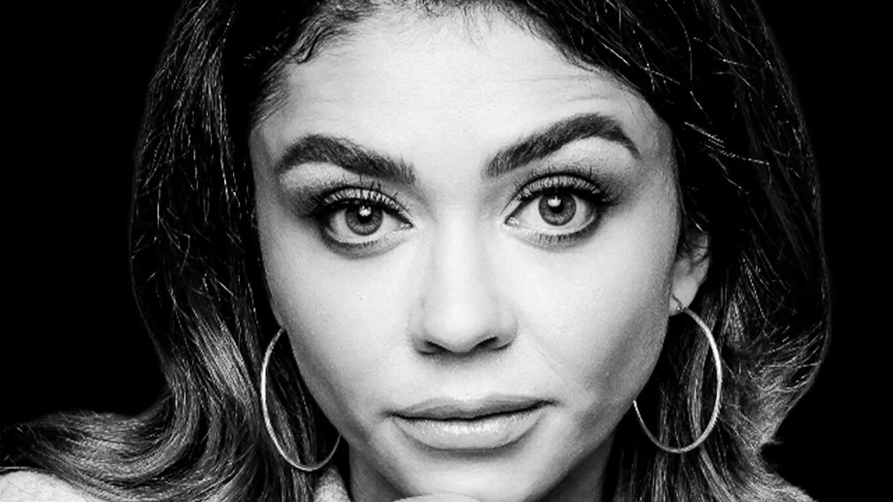 Close-up black-and-white portrait of a woman with large hoop earrings looking at the camera.