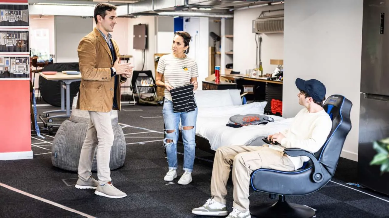 Andy Sandberg, Janette Manrara and Noah Schnapp in rehearsal for Affluenza. Set in a bedroom with a young man seated in a gaming chair while a man and woman stand talking beside the bed