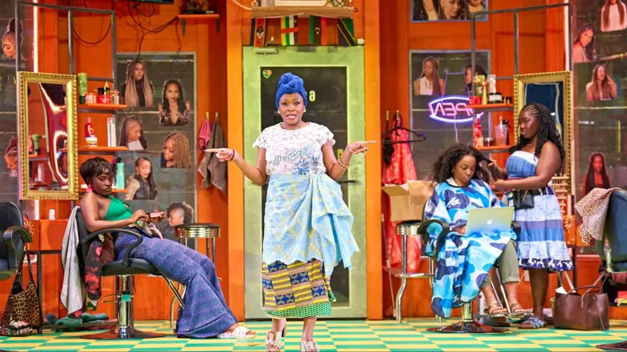 A woman in a blue headwrap gestures centre stage in a colourful Harlem hair braiding salon, with other cast members styling hair around her.