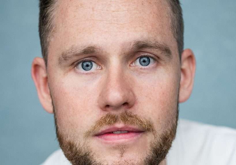 Close-up of a man with blue eyes and light brown beard looking at the camera.