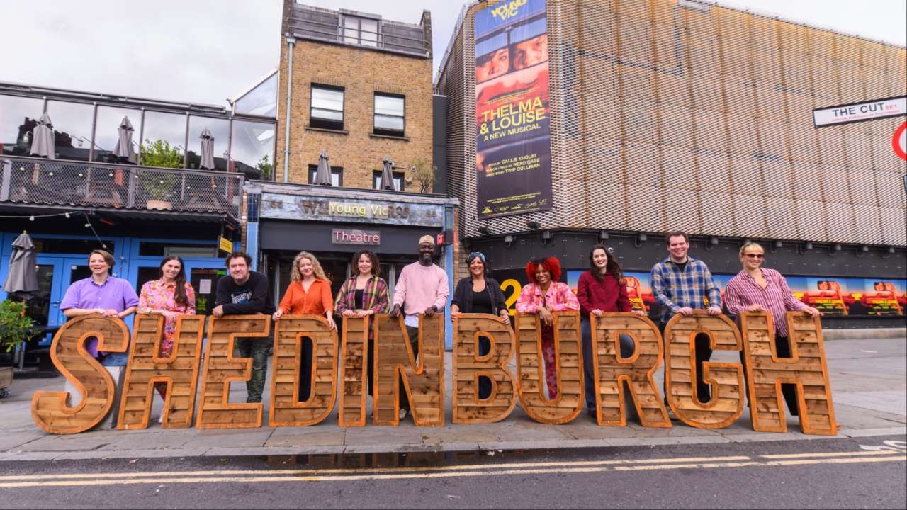 Several performers stood in a street holding signage in front of them saying: 'Shedinburgh'