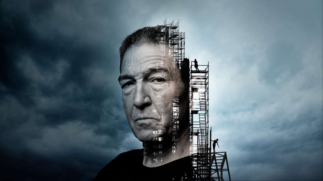Greg Hicks in The Master Builder - head and shoulders image of a white man placed on top of a building being built