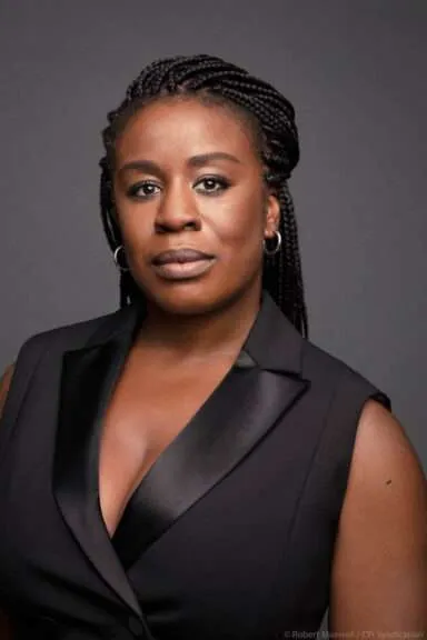 Professional head-and-shoulders portrait of a Black woman with braided hair, wearing a black blazer against a gray studio background.