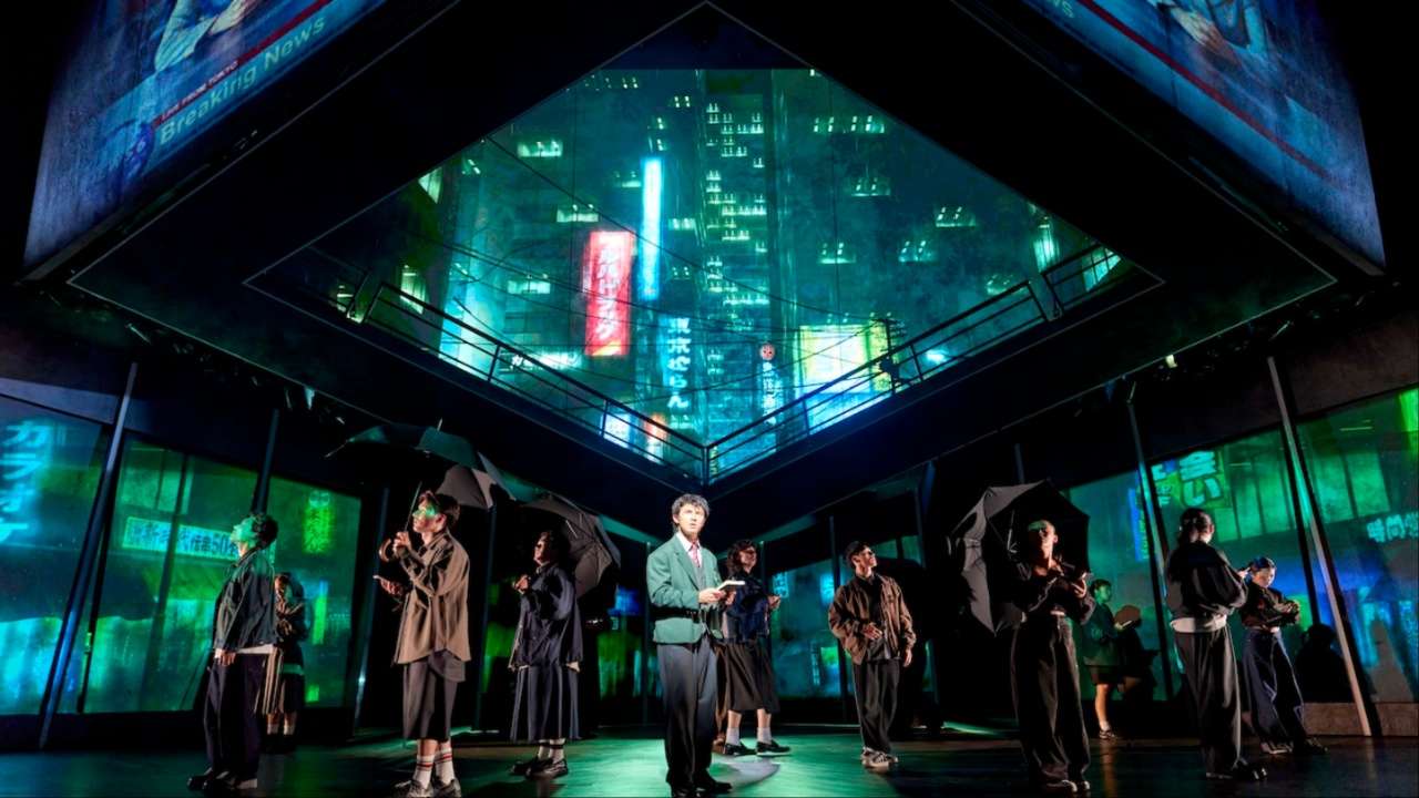 Xander Pang as Light Yagami stands centre stage in Death Note: The Musical, surrounded by an ensemble with umbrellas beneath a striking neon Tokyo cityscape projection