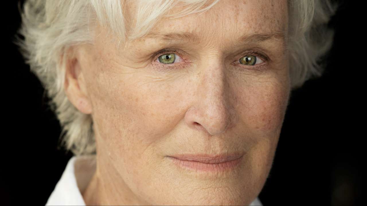 Close-up portrait of an older woman with short white hair and green eyes, neutral expression.