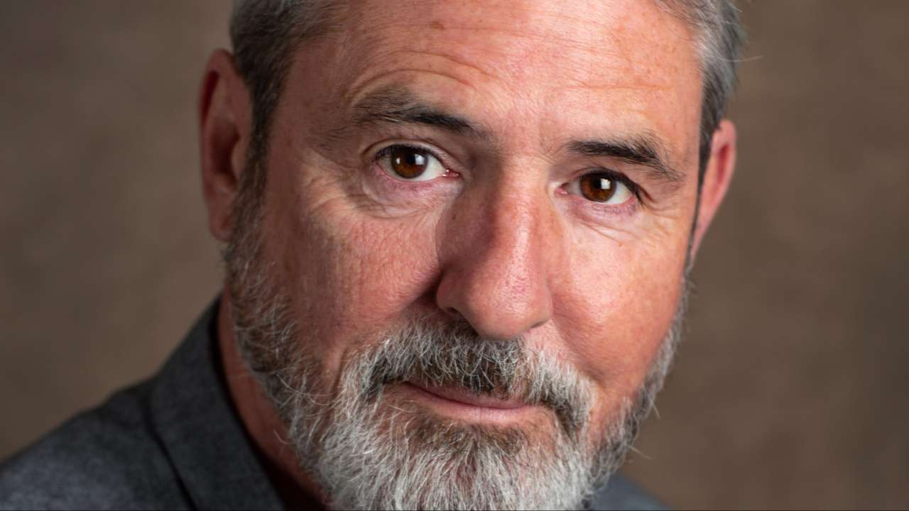 Close-up portrait of a middle-aged man with a gray beard and warm brown eyes, looking into the camera.