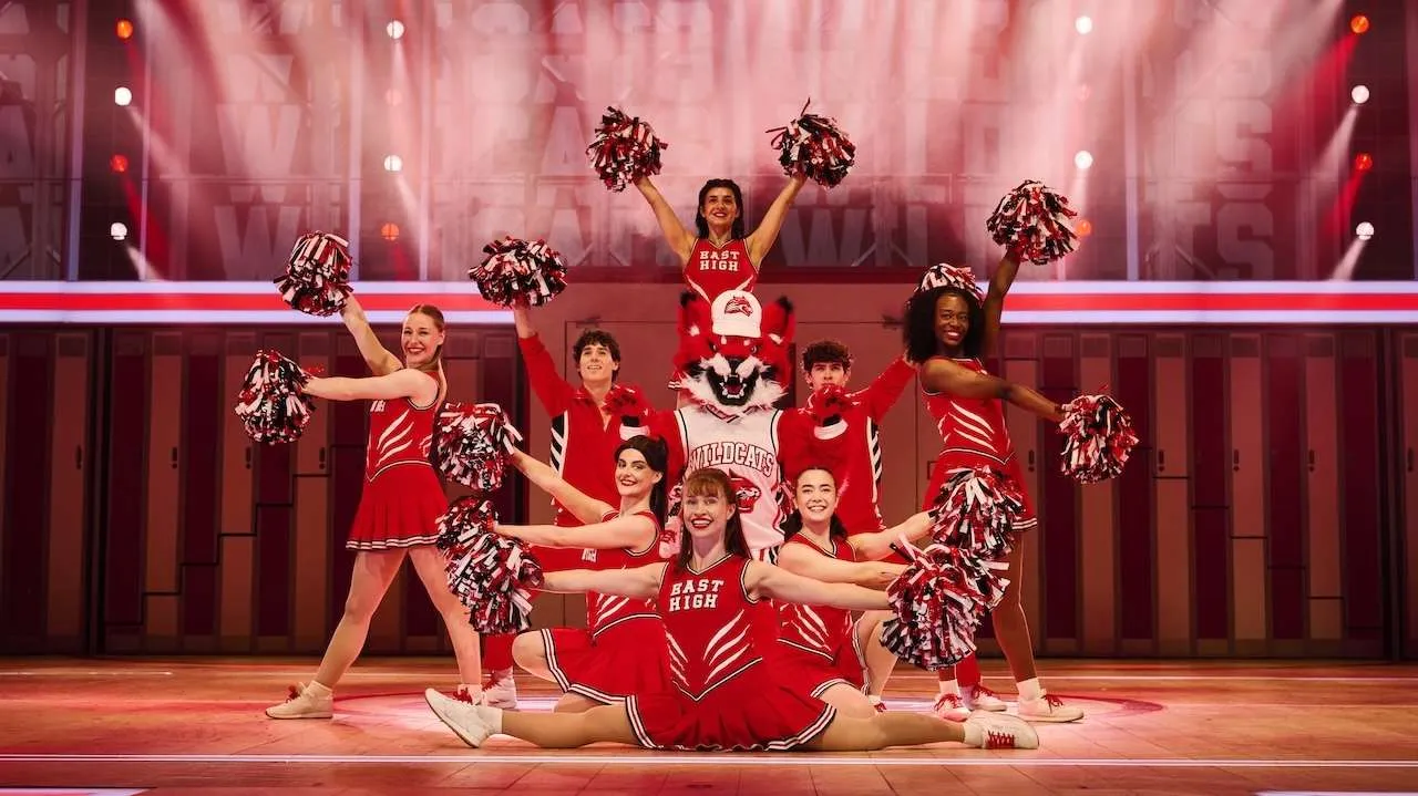 Cheerleaders in red uniforms pose on a stage with a wolf mascot center, pom-poms raised in a pyramid formation.